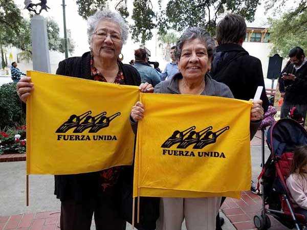 Photo of two smiling women holding flags displaying the words "Fuerza Unida."