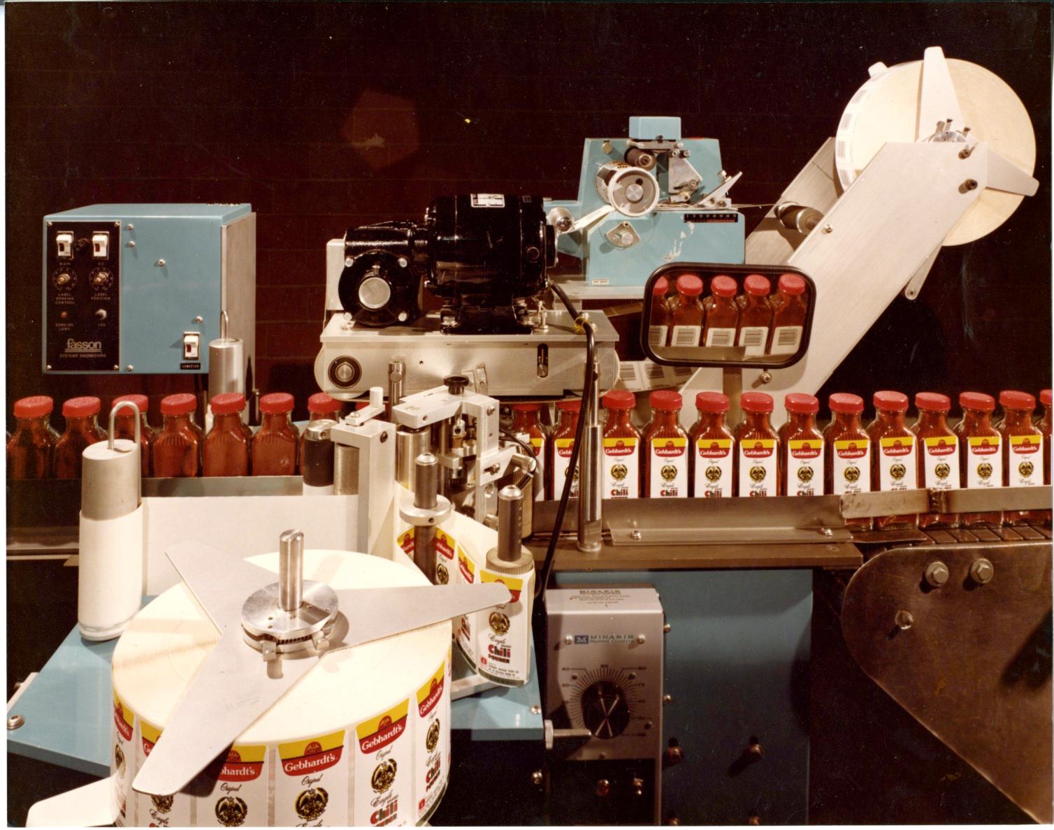 Machine adding labels to chili powder bottles